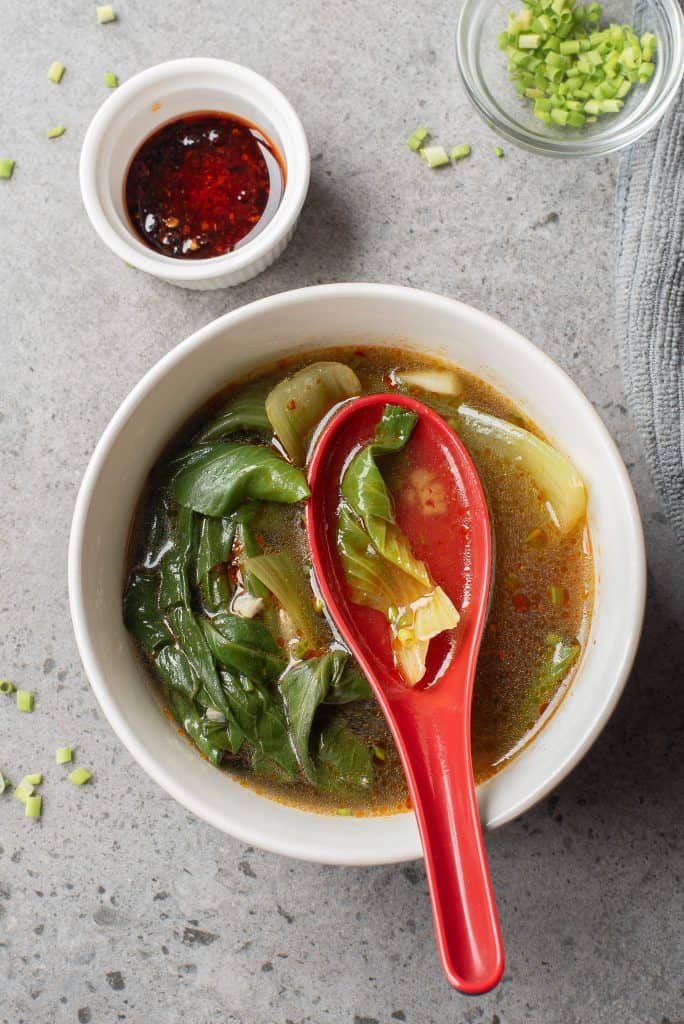 Overhead view of Bok Choy Soup with red ladle spoon in it.