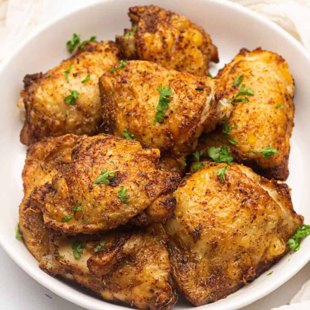 Overhead view of air fryer chicken thighs on a white plate.