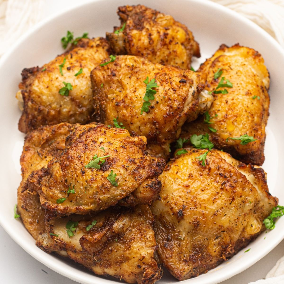 Overhead view of air fryer chicken thighs on a white plate.