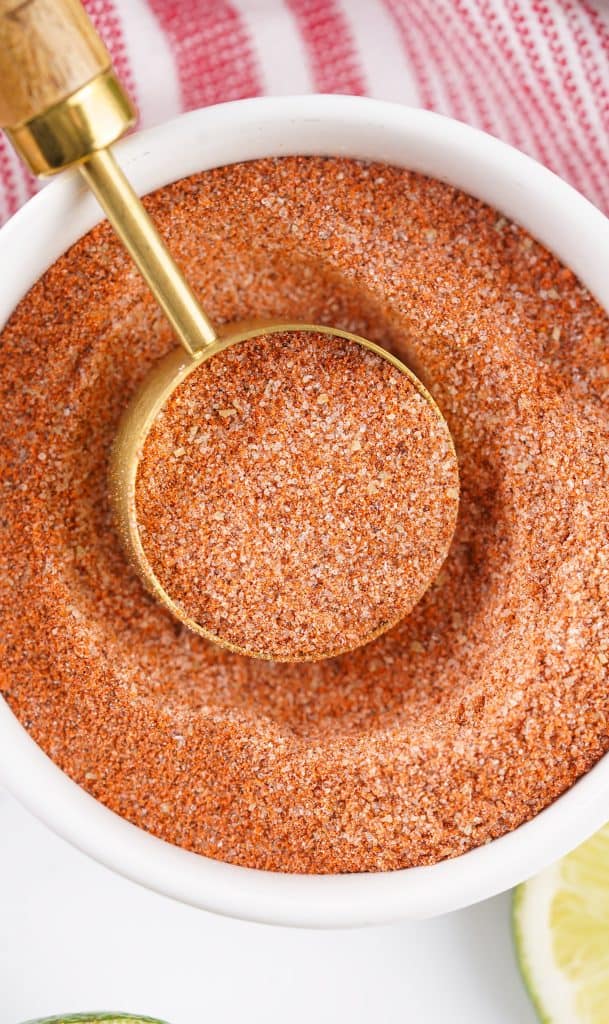 Tajin seasoning in a white bowl with a measuring spoon in it