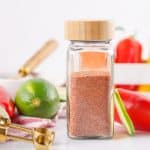 Tajin seasoning in a clear glass spice bottle.