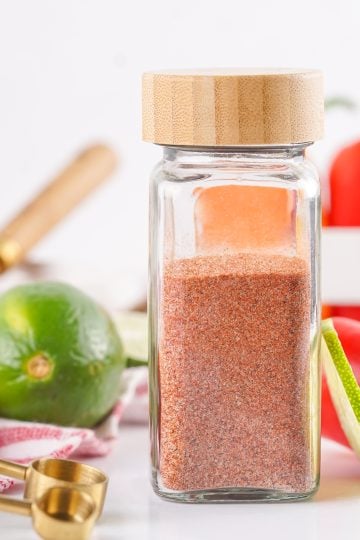 Tajin seasoning in a clear glass spice bottle.