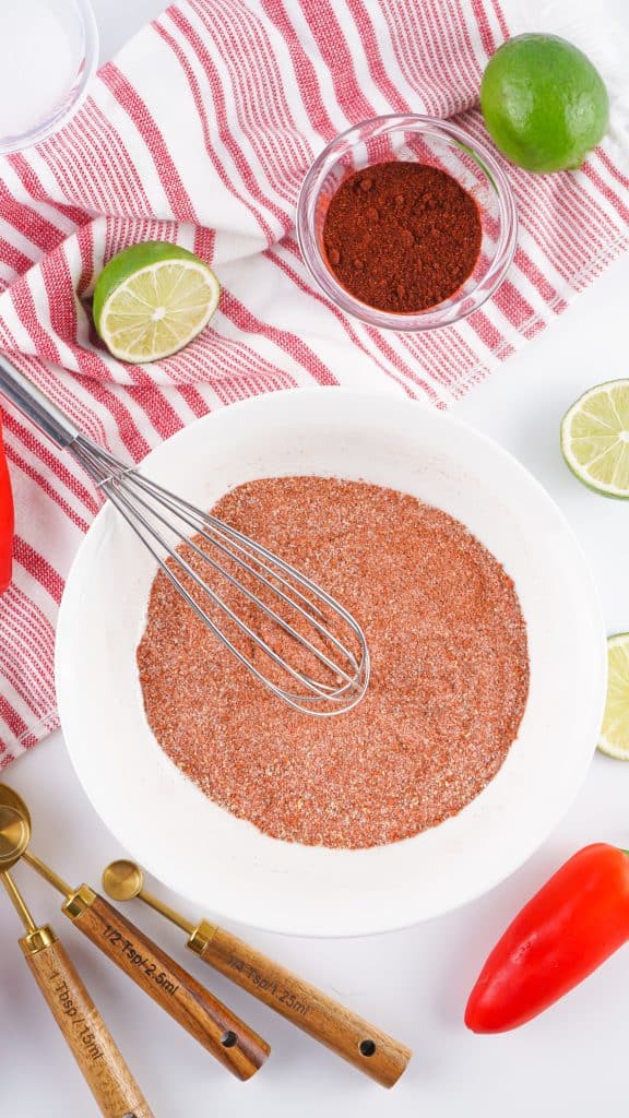 Overhead view of copycat tajin seasoning in white bowl with a whisk.