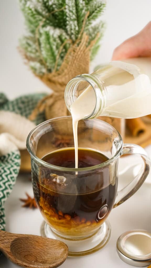Pouring eggnog coffee creamer into a glass cup of black coffee.