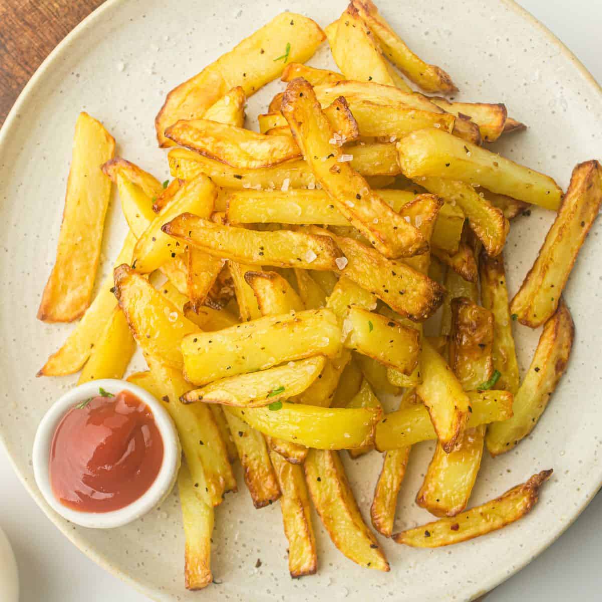 Overhead view of crispy French fries on a white plate with ketchup.