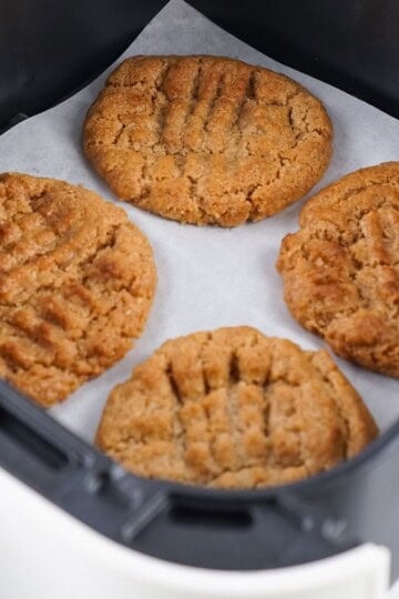 Overhead view of almond butter cookies on parchment paper in an air fryer basket.