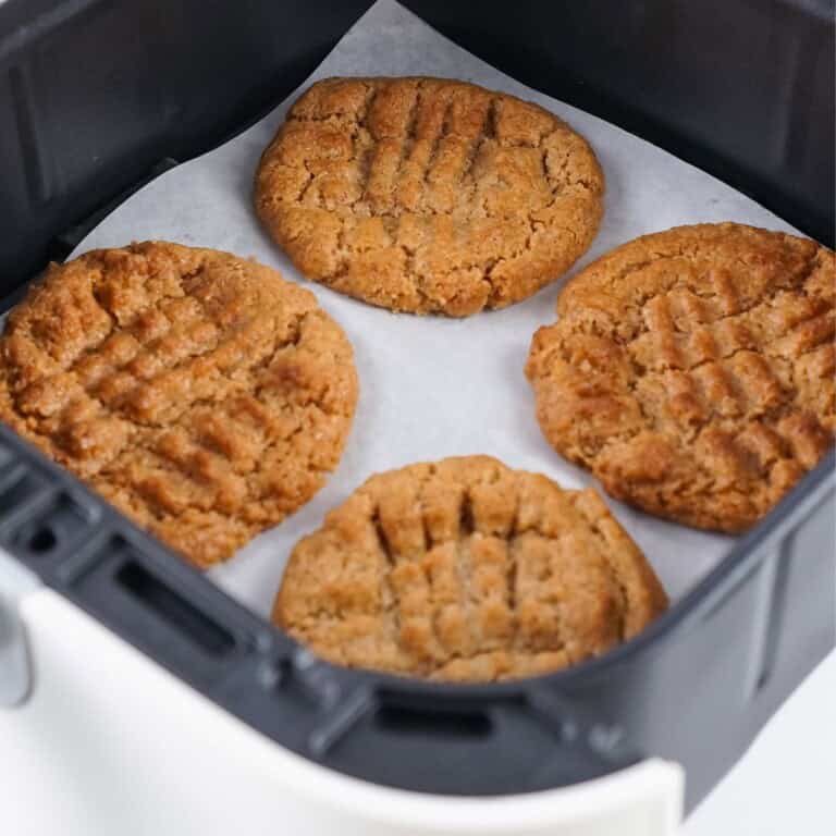 Overhead view of almond butter cookies on parchment paper in an air fryer basket.