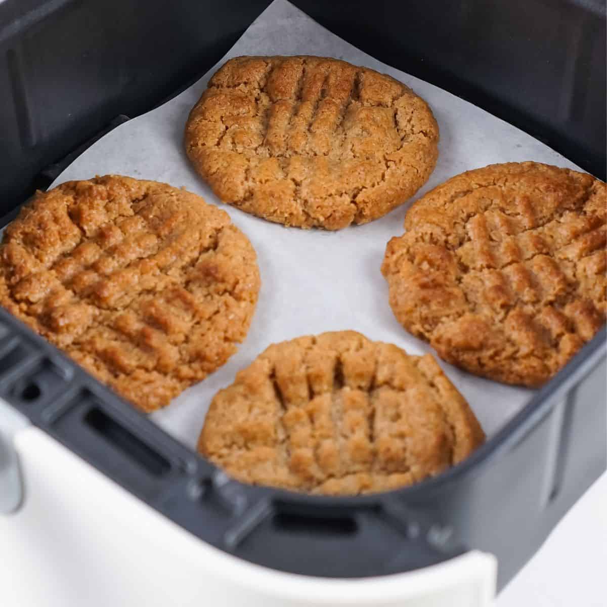 Overhead view of almond butter cookies on parchment paper in an air fryer basket.