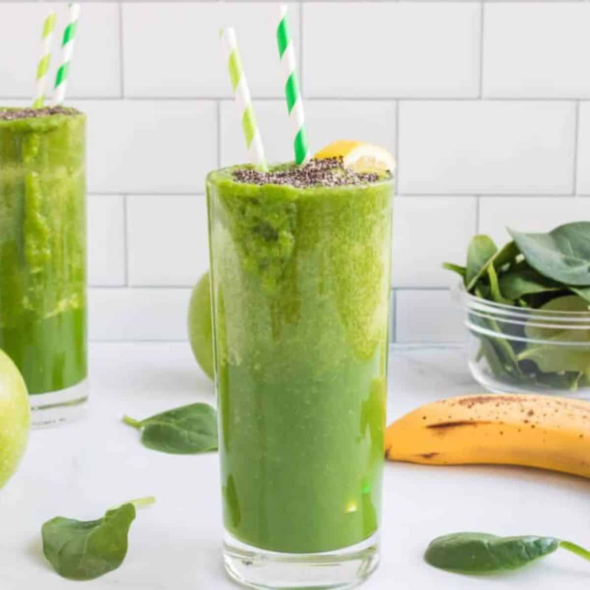 Green Apple Smoothie with striped straws in it and a lemon wedge and chia seeds on top.