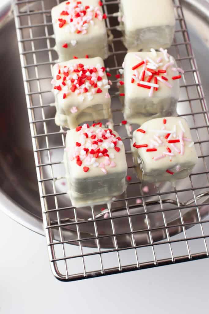Adding sprinkles to white chocolate covered brownie bites.