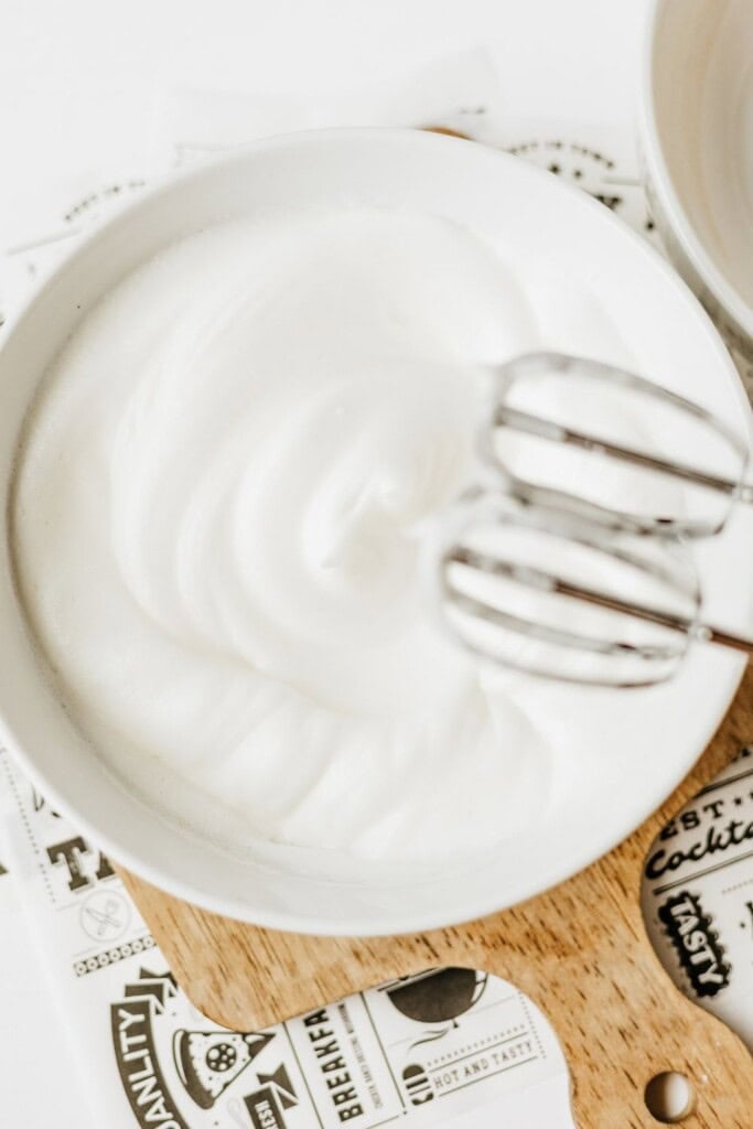 Egg whites whipped to glossy stiff peaks with mixer beaters resting in the bowl