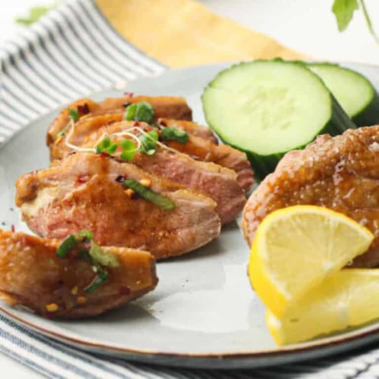 Crispy Air Fryer Duck on a white plate with lemon slices.