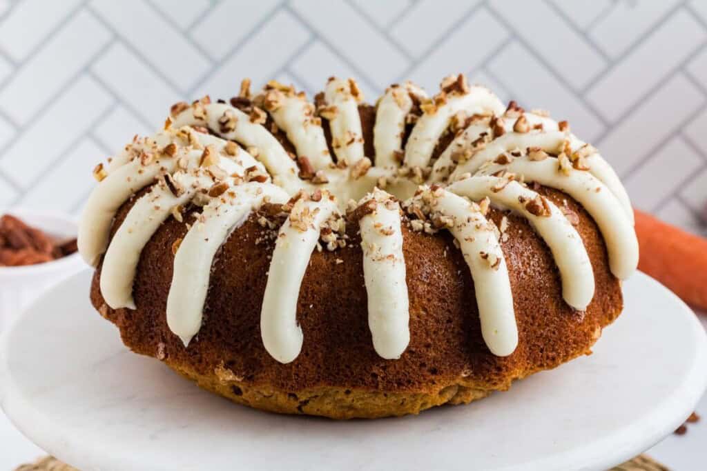 Copycat Nothing Bundt carrot cake on a cake stand with cream cheese frosting petals
