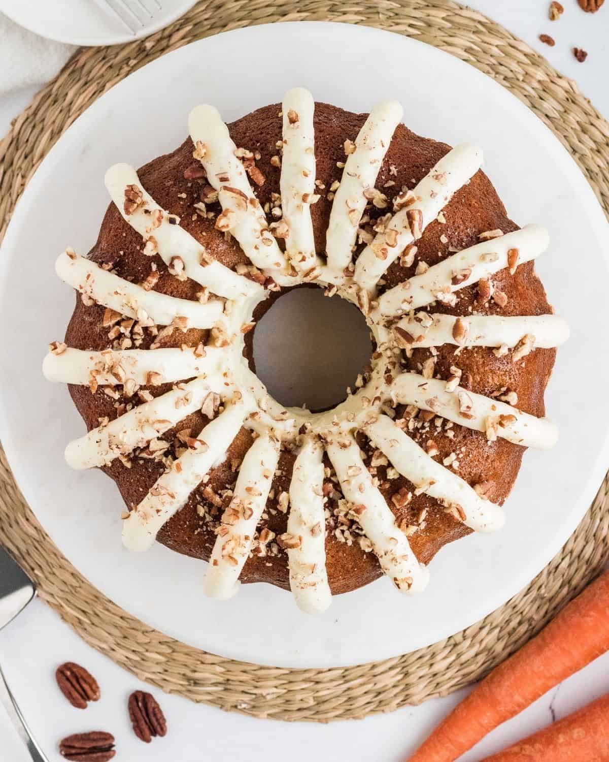 Copycat Nothing Bundt Cake carrot cake with cream cheese frosting and chopped pecans on a white plate
