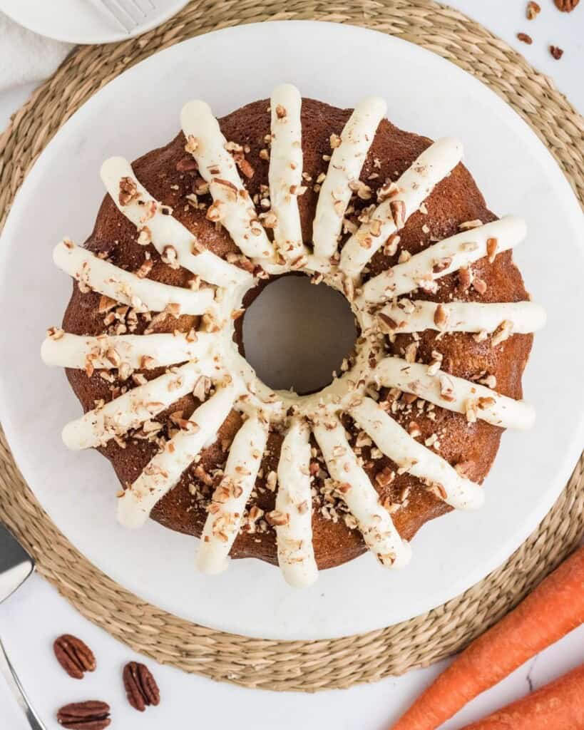 Copycat Nothing Bundt Cake carrot cake with cream cheese frosting and chopped pecans on a white plate