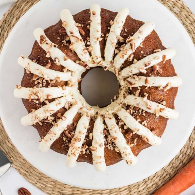Copycat Nothing Bundt Cake carrot cake topped with cream cheese frosting petals and chopped pecans