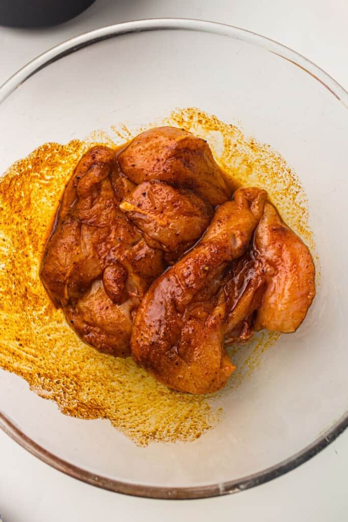 overhead view of chicken breasts in a large glass bowl marinated with spices and drizzled with olive oil.