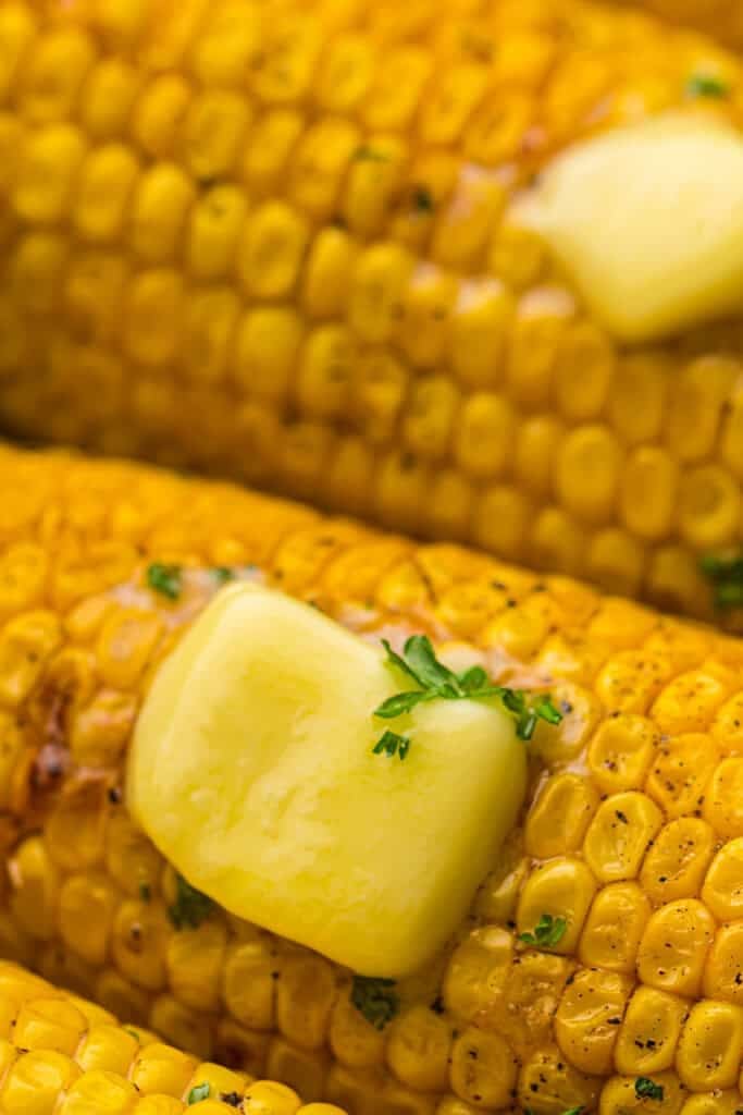 overhead view and closeup o charred corn with melting pat of butter and sprinkled parsley