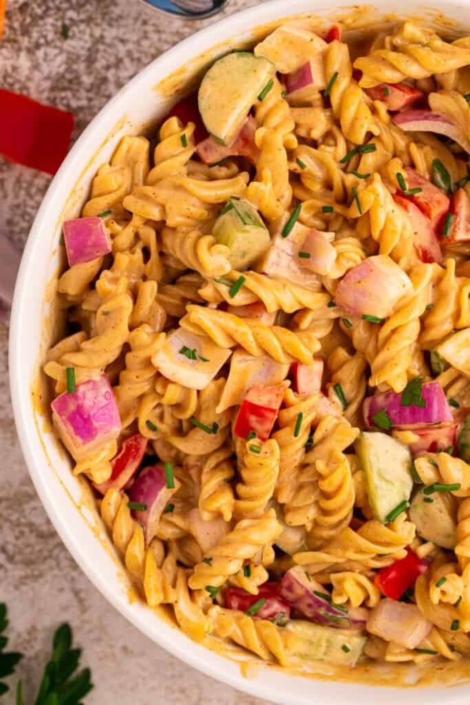 Close-up of creamy BBQ pasta salad showing rotini coated in tangy BBQ dressing with diced red bell pepper, English cucumber, red onion, and chopped chives