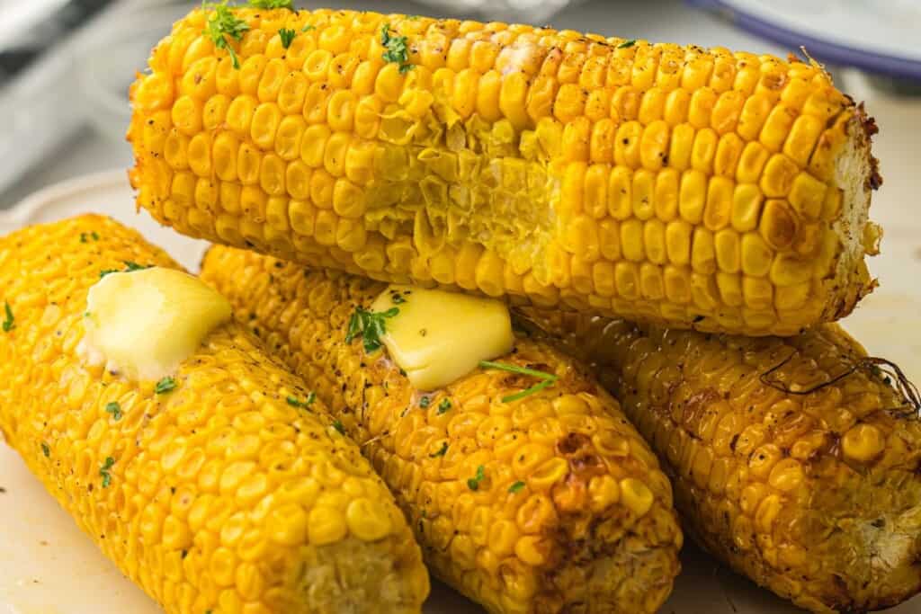 corn on cob with a bite out of it stacked on 3 other ears of crn with melted butter