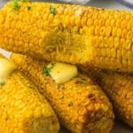 corn on cob with a bite out of it stacked on 3 other ears of crn with melted butter