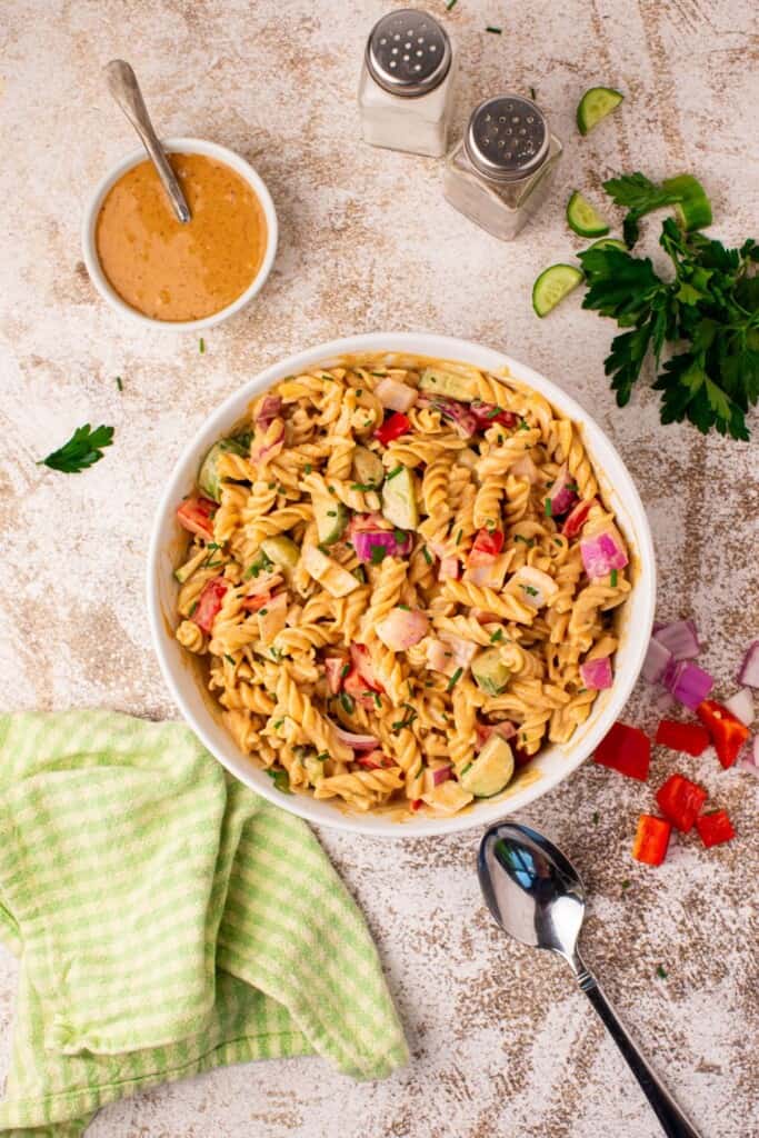 Creamy BBQ pasta salad in a white serving bowl with rotini, bell pepper, cucumber, red onion, and fresh chives, served as a summer cookout side dish