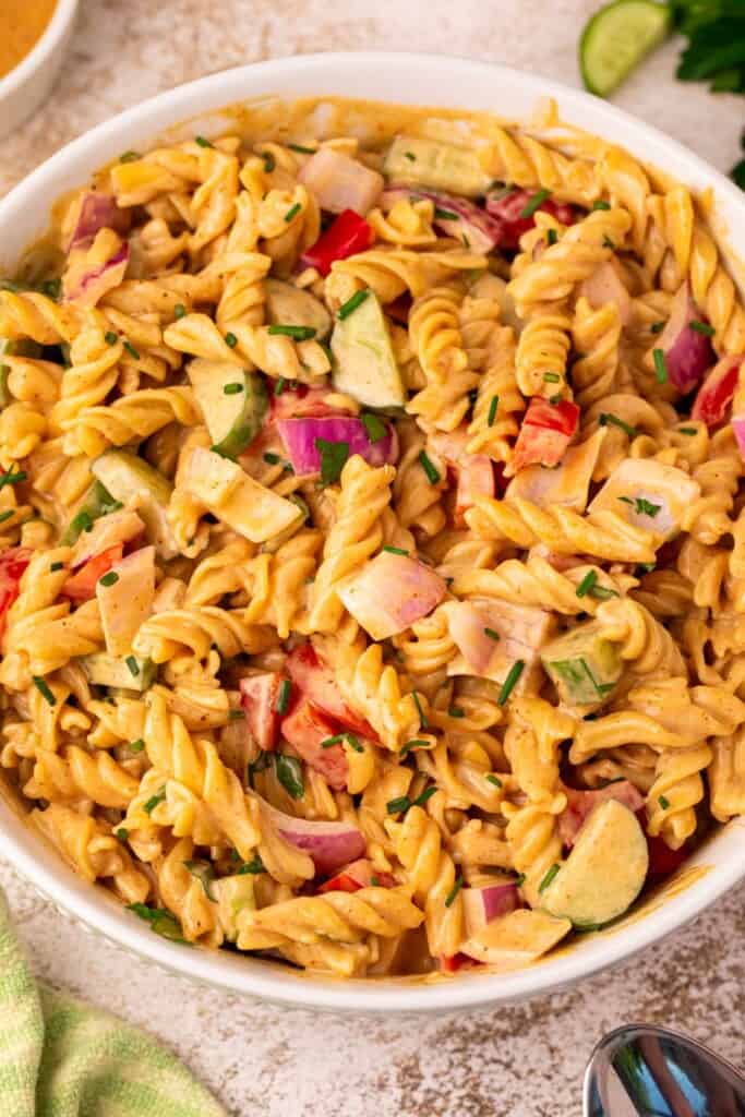 Creamy BBQ pasta salad tossed together in a large mixing bowl with rotini, bell pepper, cucumber, red onion, and chives evenly coated in tangy BBQ dressing