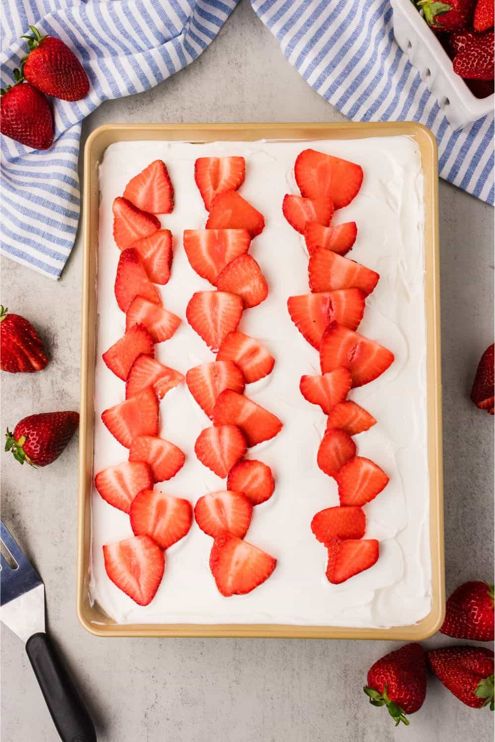 Fresh strawberry cake topped with whipped coconut cream and sliced fresh strawberries in 9x13 pan