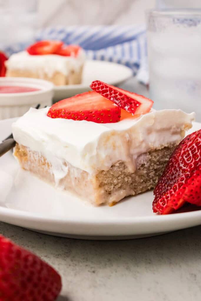 Slice of fresh strawberry cake with whipped coconut cream and fresh strawberries on top