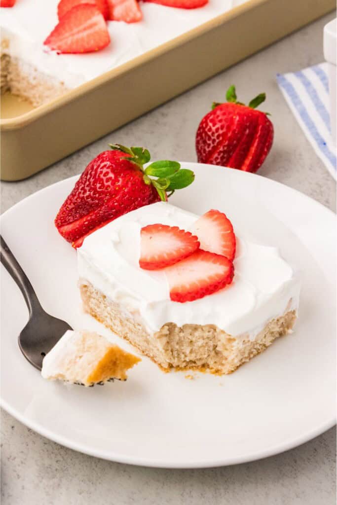 Slice of fresh strawberry cake on white plate with sliced strawberries