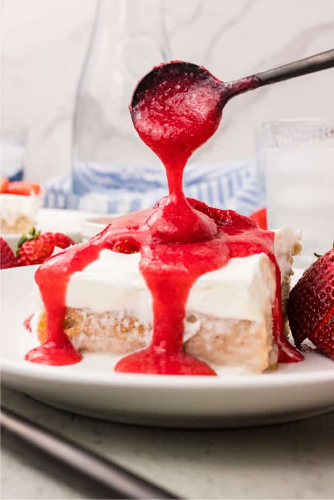 Fresh strawberry cake slice with strawberry purée drizzled on top with a black spoon