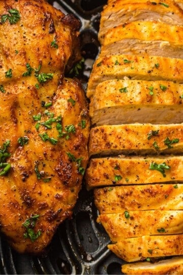 overhead view of air fryer chicken breast and sliced air fryer chicken breast in ar fryer basket.