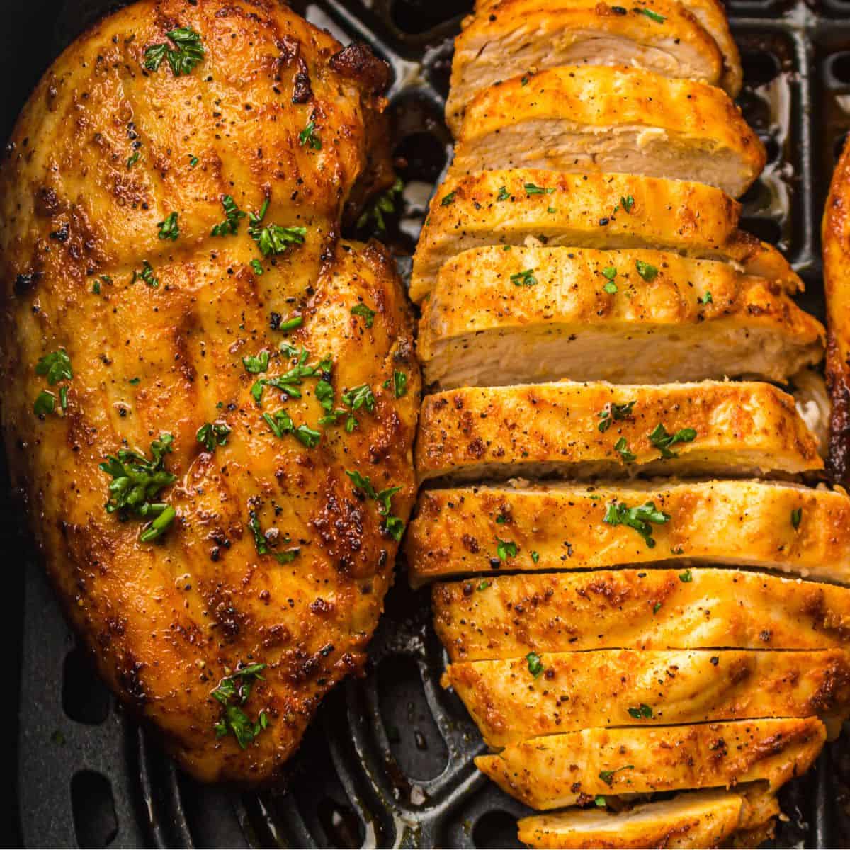 overhead view of air fryer chicken breast and sliced air fryer chicken breast in ar fryer basket.