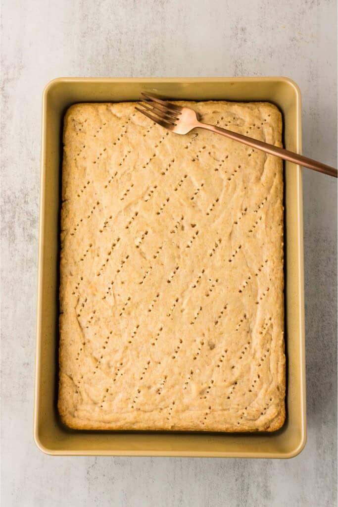 Baked gluten-free strawberry cake with fork holes ready for the strawberry milk soak