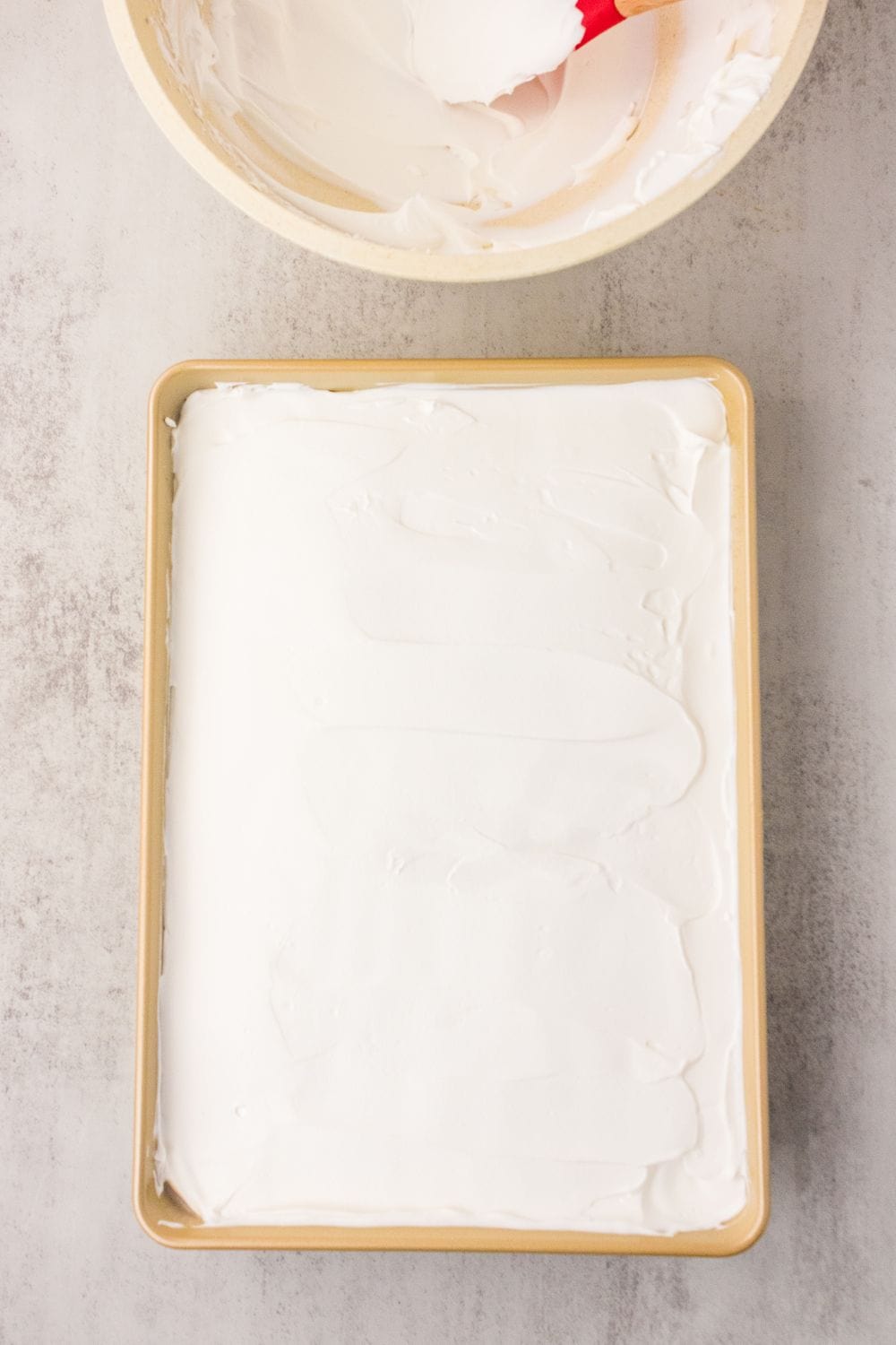 Whipped coconut cream spread over chilled strawberry cake in 9x13 pan