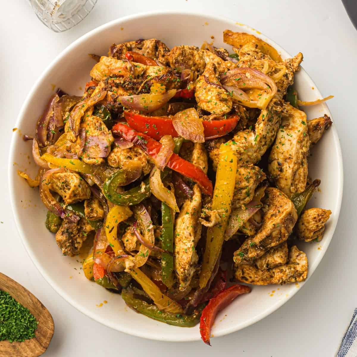 Bowl of air fryer chicken fajitas garnished with parsley and lime featured image