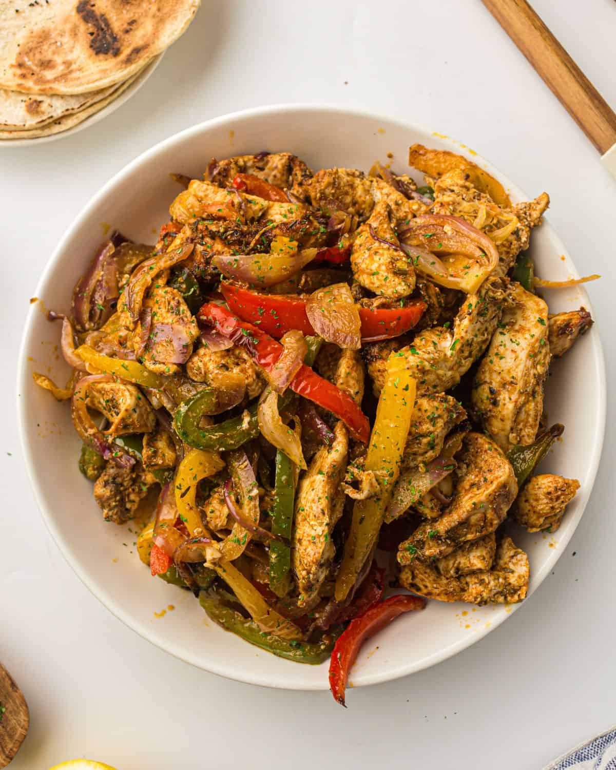 Air fryer chicken fajitas served in a white bowl with warm tortillas