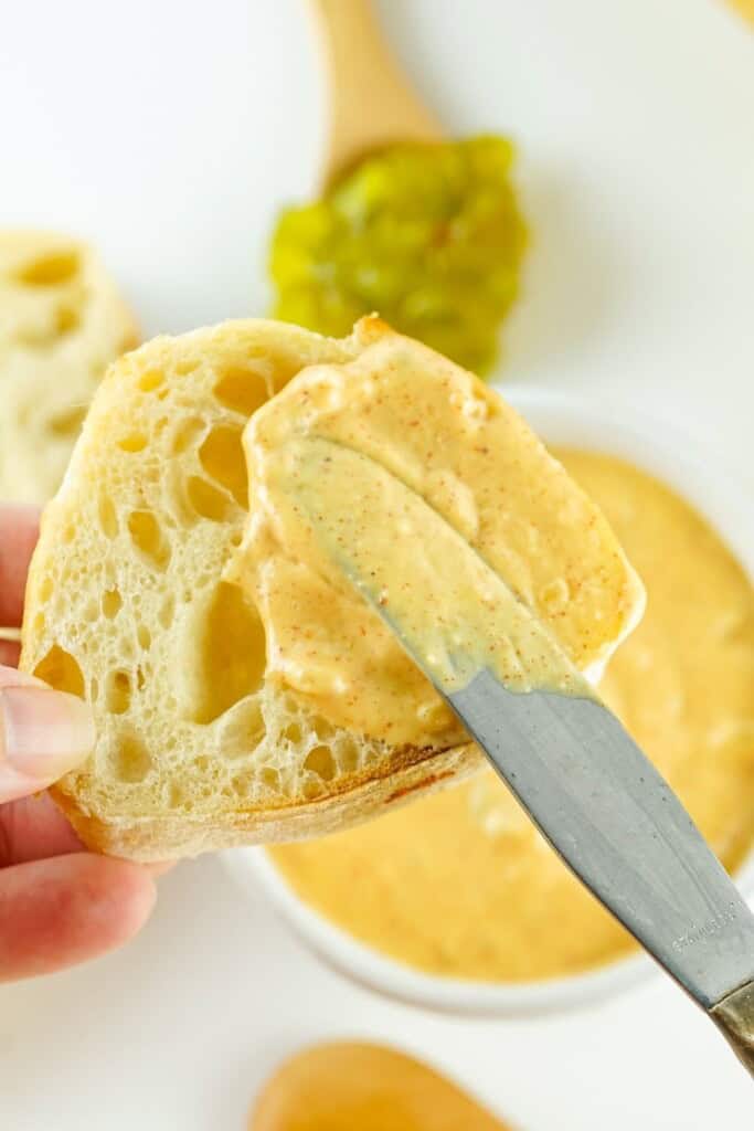 Hand spreading creamy copycat Big Mac sauce onto a slice of crusty bread