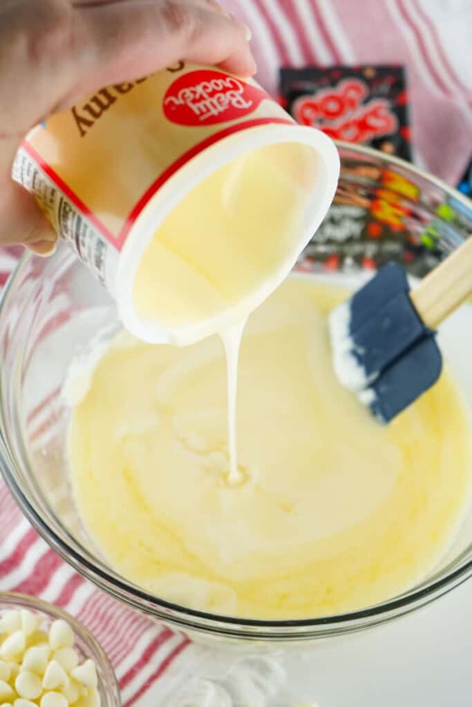 Pouring warm vanilla frosting into melted white chocolate to make fudge