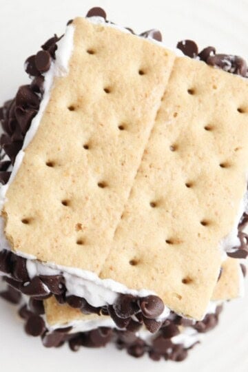 Overhead view of a stack of frozen s'mores coated in mini chocolate chips on a white plate.
