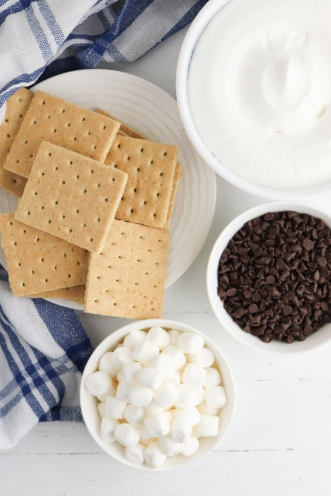 Ingredients for frozen s'mores including graham crackers, whipped topping, mini marshmallows, and mini chocolate chips.