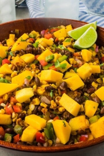 mango black bean salad with two lime wdges in a wooden bowl