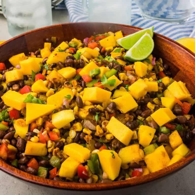 mango black bean salad with two lime wdges in a wooden bowl