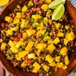 Mango black bean salad with lime wedges on top in a large wooden serving bowl