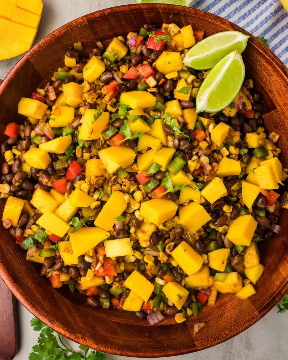 Mango black bean salad with lime wedges on top in a large wooden serving bowl