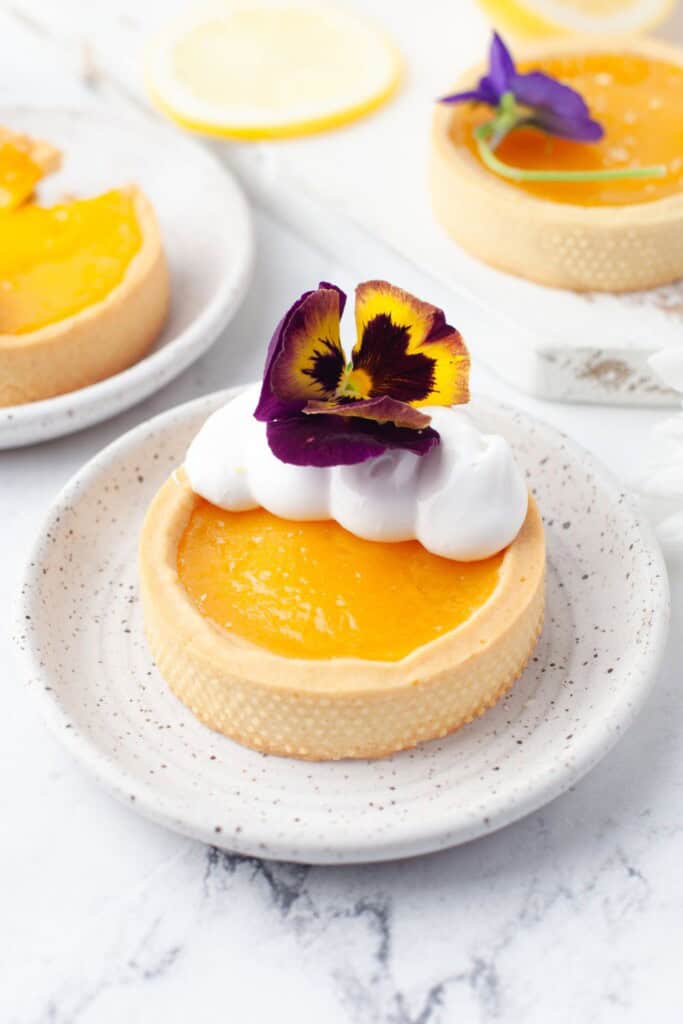 Individual lemon meringue tartlets with meringue, edible pansies, and fresh lemon slices