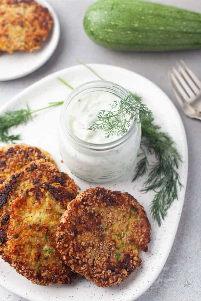overhead view of crispy zucchini patties with tzatziki sauce on the side