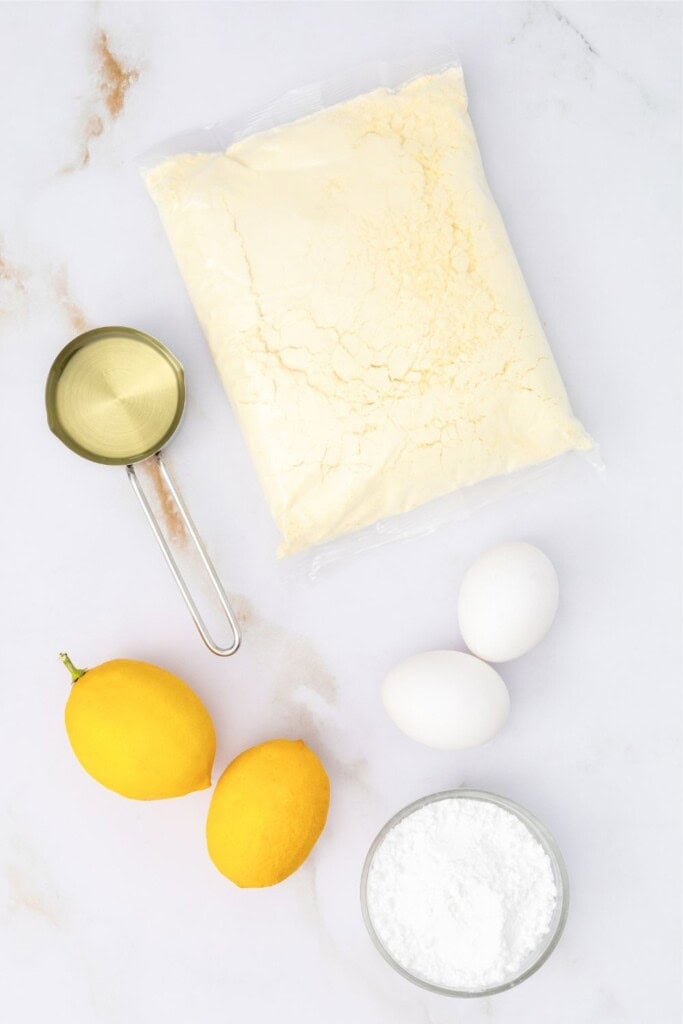 Ingredients for lemon crinkle cookies including lemon cake mix, eggs, oil, fresh lemons, and powdered sugar