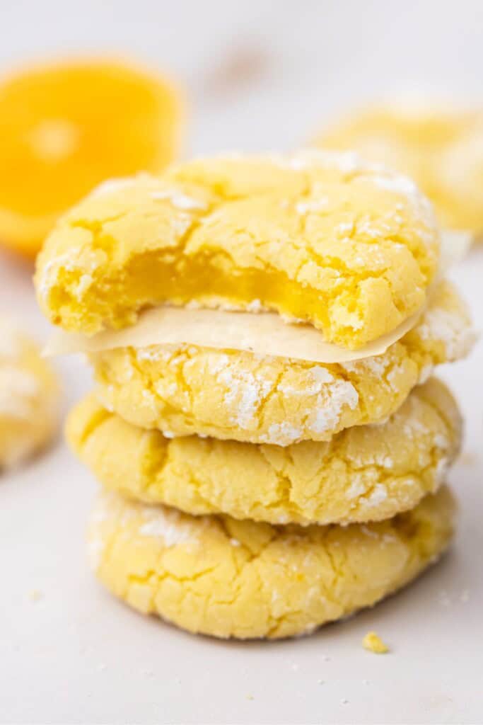 Stack of lemon crinkle cookies with a bite showing the soft lemon center