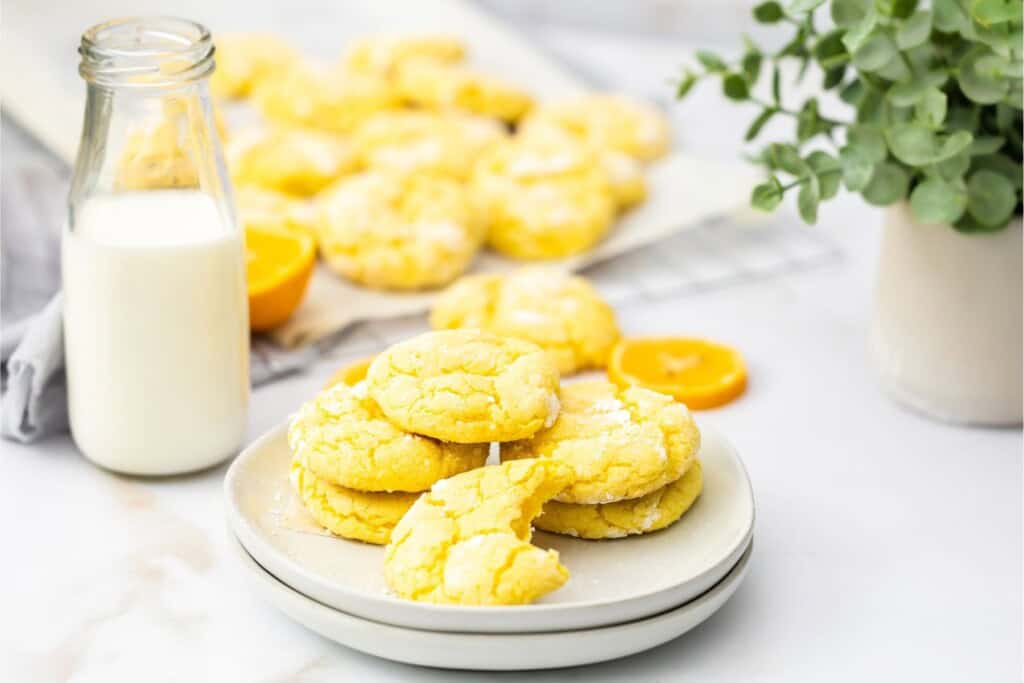 Lemon crinkle cookies with cake mix stacked on a white plate with a bottle of milk
